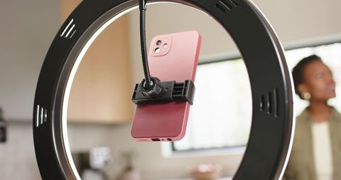 Vlogger filming with pink smartphone in ring light in bright kitchen