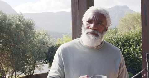 Senior man reflecting while holding mug in outdoor garden setting