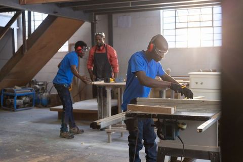 African american woodworkers operating table saw in industrial workshop assembling cabinets