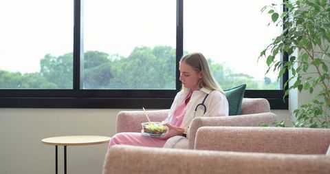 Female clinician eating salad during break in bright clinic lounge