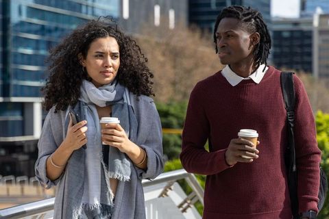 Multicultural friends walking promenade holding takeaway coffee and checking smartphone