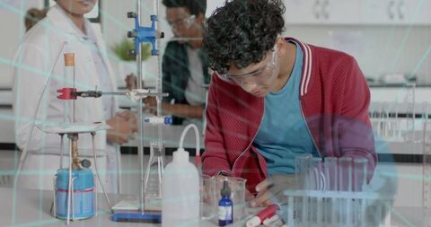 Teen measuring beaker in school chemistry lab wearing safety goggles and working with burner