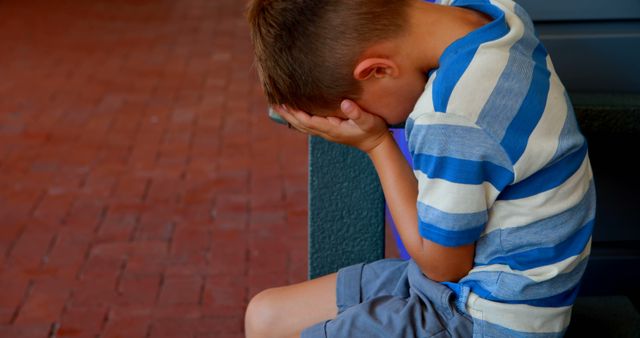A distressed young boy sits with his head in hands, embodying sadness or frustration. - Download Free Stock Photos Pikwizard.com