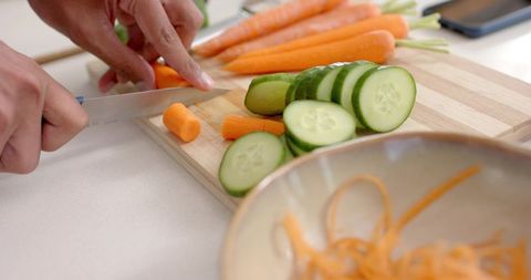 African-american man slicing cucumber and carrot on wooden board for healthy meal prep
