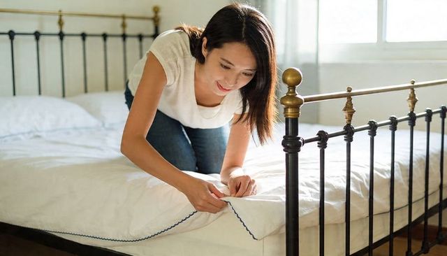 Young woman smoothing sheets on iron bed in sunlit minimalist bedroom, peaceful morning