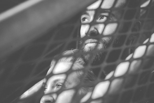 Couple standing behind netting, creating a pattern of shadows on their faces. Black and white tone emphasizes their thoughtful expressions. Perfect for themes of contemplation, intimacy, emotional connection, or thoughtful moments, suitable for publications on relationships, mental health, and emotional well-being.