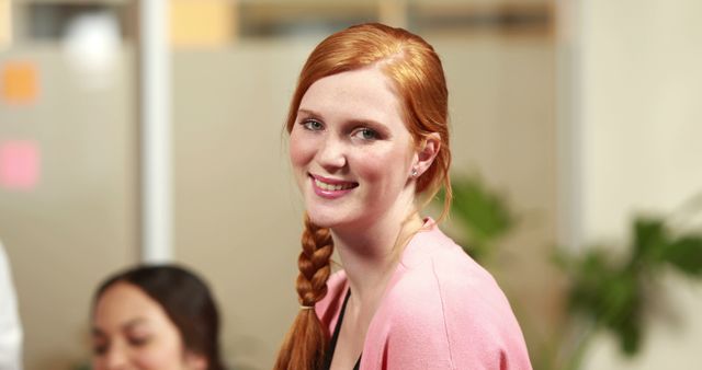 A young Caucasian woman with red hair smiles at the camera, with copy space. Her professional attire suggests she could be in a business or office environment.