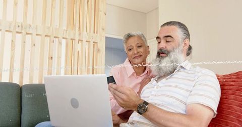Mature couple making online payment with credit card and laptop in cozy modern living room