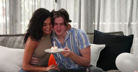 Interracial couple celebrating birthday with candlelit cupcake