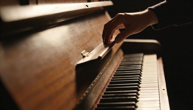 Hand lifting fallboard on vintage upright piano in moody low light