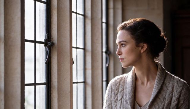 Thoughtful woman gazing out mullioned window in historic stone interior, soft natural light