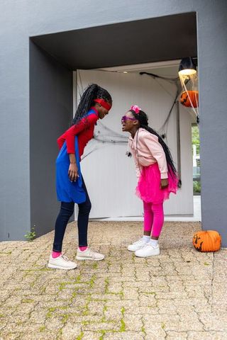 Playful african american girls wearing bright halloween costumes laughing on porch