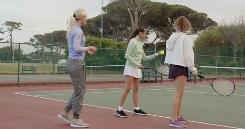 Women practicing tennis serves on public park court during overcast day group training