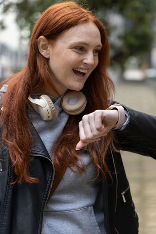 Redhead woman checking smartwatch while laughing, wearing headphones and leather jacket