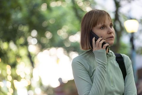 Young woman talking on smartphone while standing in urban park with backpack