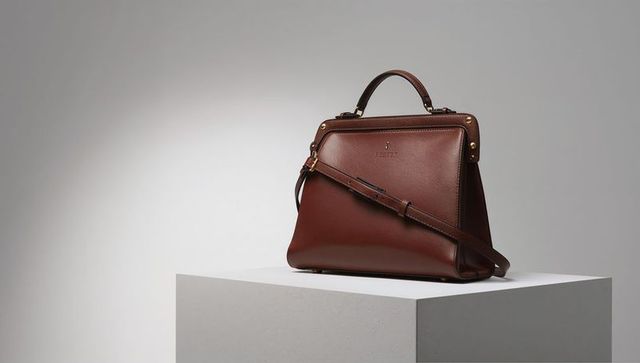 Showcasing structured brown leather handbag with gold hardware on minimalist white plinth