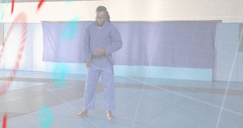 Male Martial Artist Tying Belt in Blue Gi on Dojo Mats Demonstrating Focus and Discipline