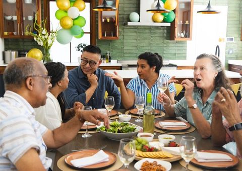 Multigenerational friends sharing meal and wine around kitchen dining table