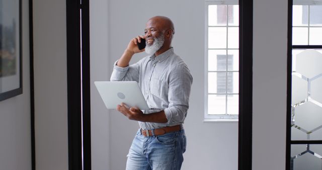 Smiling Senior Businessman Holding Laptop and Talking on Phone in Modern Office - Download Free Stock Images Pikwizard.com