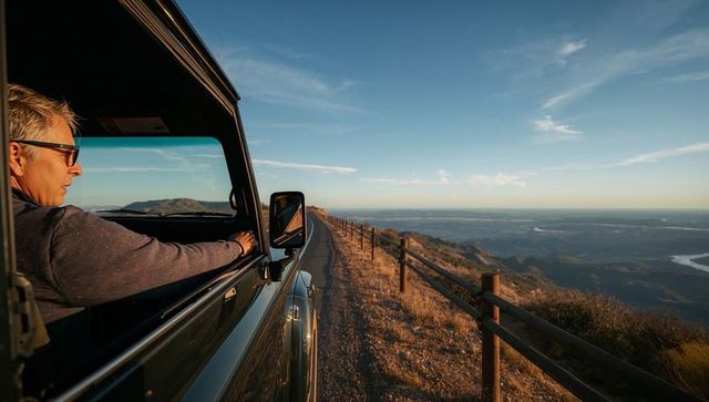 Middle-aged man driving suv along mountain ridge at sunset leaning out window enjoying view