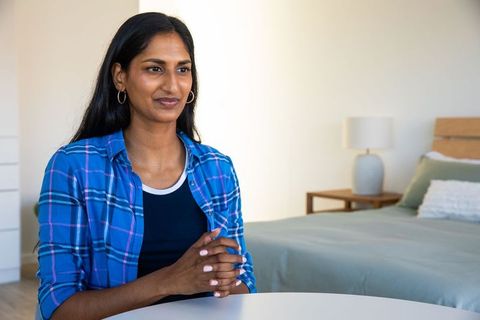Thoughtful Indian Woman Clasping Hands at Table in Minimal Bedroom