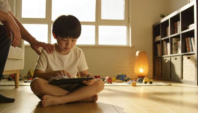 Child sitting on floor using tablet while parent supervising in sunlit living room