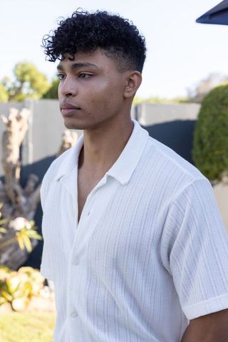 Young african american man standing in sunlit backyard gazing left wearing white shirt