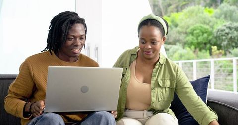African American couple sharing laptop on sofa, planning finances and shopping online