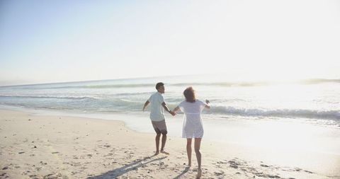 Romantic biracial couple holding hands on sunlit beach