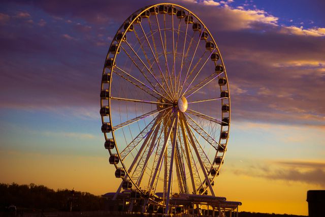 Colorful image of a Ferris wheel during sunset with clouds in the sky, perfect for travel and tourism promotions, website banners, or background for amusement park advertisements. Captures vibrant colors and calming ambiance of evening, suitable for relaxation and leisure themes.