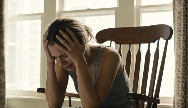 Young woman clutching head and crying in rocking chair by sunlit window
