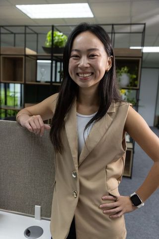Smiling professional woman leaning on cubicle in modern open-plan office with greenery