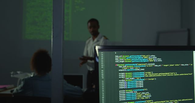 A middle-aged man is presenting in a dark room, during a coding workshop or lecture, with a focus on a computer screen displaying code in the foreground. The setting suggests an educational environment where programming skills are being taught or discussed, with copy space.