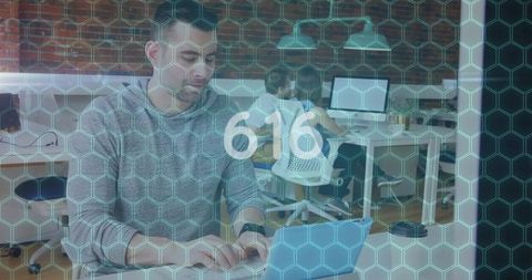 Young professional typing on laptop in collaborative office with hexagonal data overlay