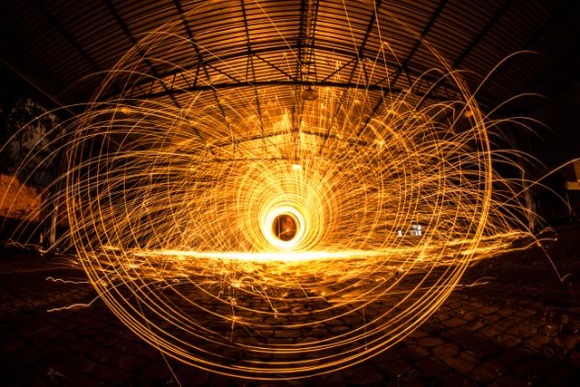Long exposure photograph capturing vibrant steel wool sparkler light painting in an industrial warehouse. Ideal for use in artistic projects, promotional materials, technology backgrounds, creative designs, or as a dynamic visual for presentations focused on art, creativity, and light manipulation.