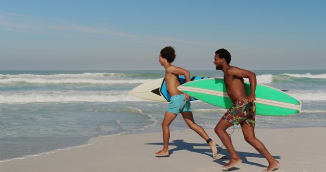 Young African American man and biracial man running on the beach. They carry surfboards, ready for an exciting day of surfing in the sun.