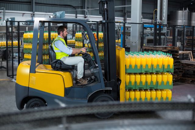 Factory worker operating forklift transporting packed juice bottles in a warehouse. Ideal for illustrating industrial operations, logistics, manufacturing processes, and the beverage industry. Useful for articles, advertisements, and educational materials related to warehouse management, safety protocols, and supply chain logistics.