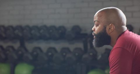African man leaning and catching breath after intense workout by dumbbell rack