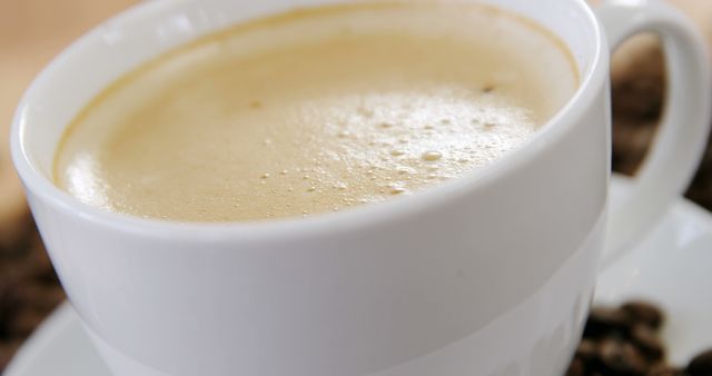 A close-up view of a freshly brewed cup of coffee in a white mug, with copy space. Its creamy surface and the scattered coffee beans in the background suggest a warm, inviting atmosphere for coffee enthusiasts.