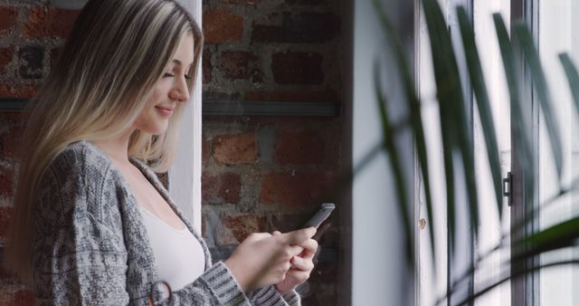 Smiling Woman Using Smartphone by Window in Cozy Room - Download Free Stock Images Pikwizard.com