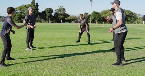 Coach leading teen athletes in throwing and catching reaction drill on sunny grass field