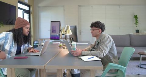 Two coworkers collaborating at modern coworking table with laptops, coffee, natural light