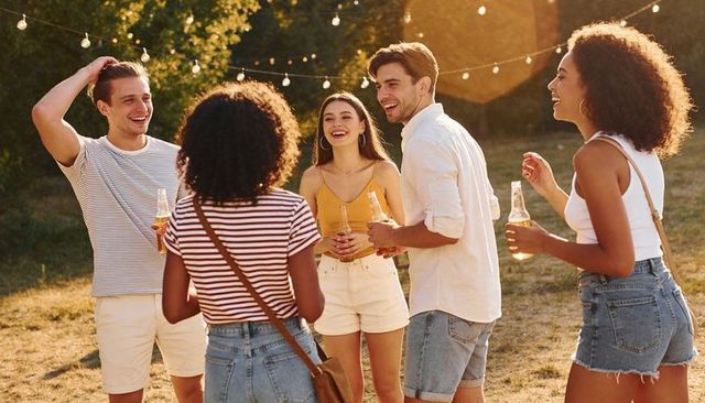Group of friends laughing and drinking at outdoor summer party under glowing string lights