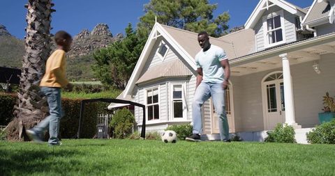 African american father and son playing soccer on sunny front lawn of charming home