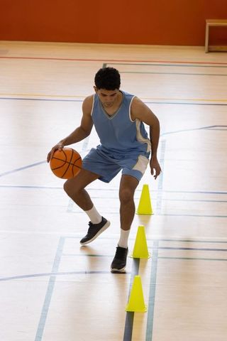 Male athlete dribbling basketball through agility cones on indoor court training