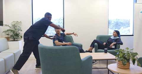 Healthcare team relaxing and chatting in modern staffroom with teal armchairs and greenery