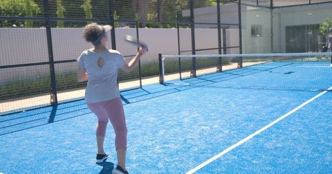 Active woman swinging paddle on vibrant blue padel court wearing visor and leggings