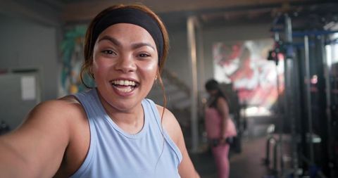 Energetic women taking fitness selfie at gym with dumbbells and colorful mural backdrop
