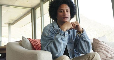 African american man sitting on sofa in modern living room wearing denim jacket