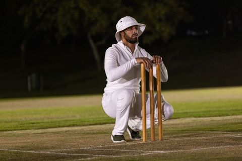 Kneeling cricketer holding wickets on night pitch under floodlights